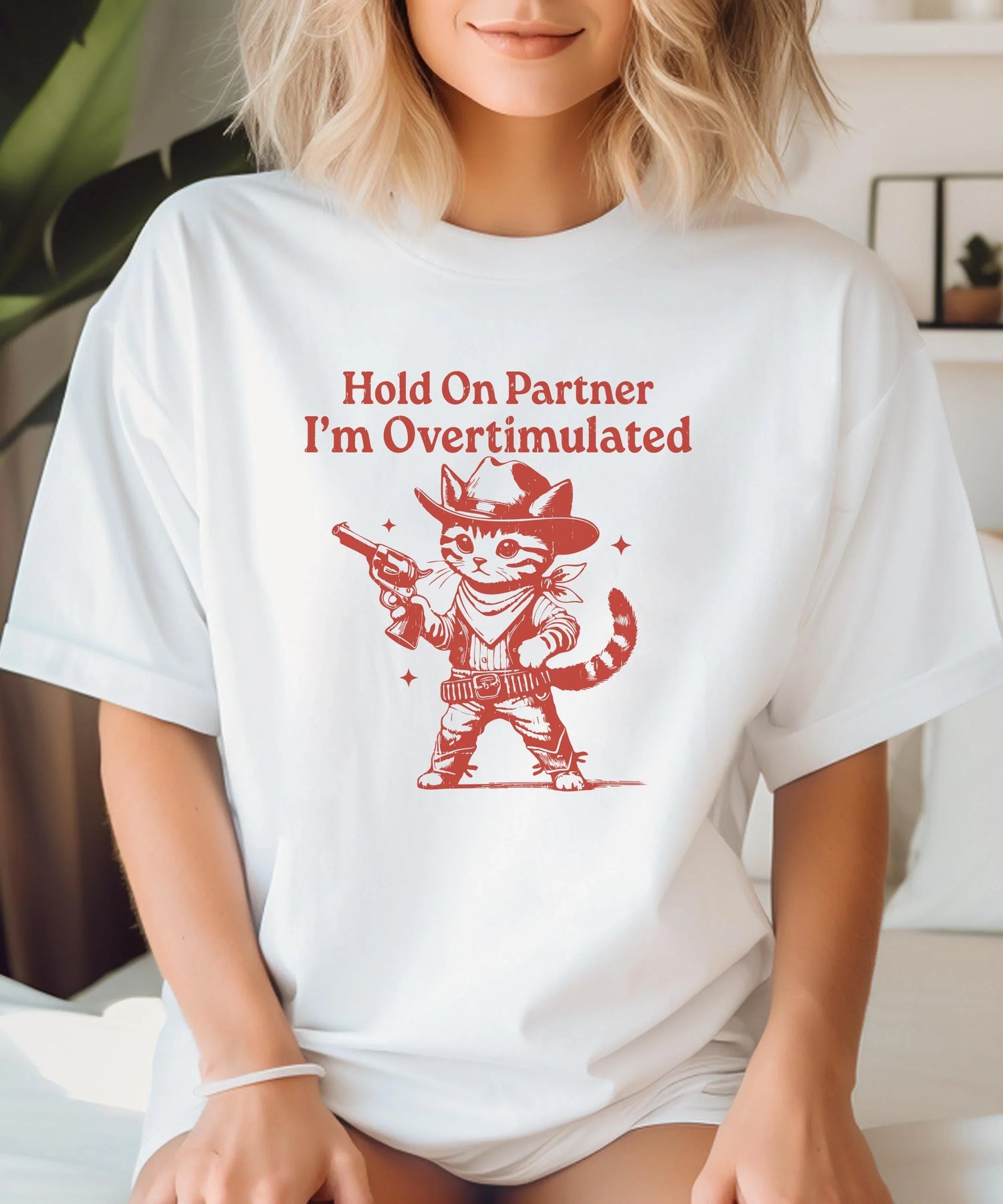 Cowgirl themed t-shirt featuring a playful cat in cowboy attire with the text "Hold On Partner I'm Overstimulated".